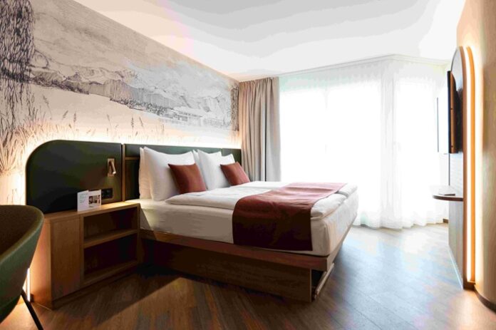 Hotelzimmer mit Doppelbett halbhoher dunkler Wandverkleidung und grafischem Gebirgedessin darüber