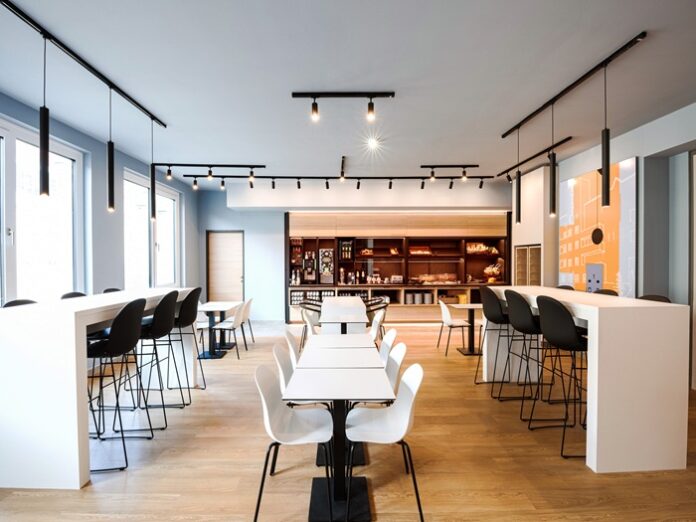 Raum mit langer Tafel in der Mitte und Tischen mit Barstühlen an den beiden Seiten
