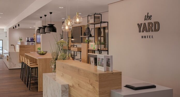 Helles Holz und dunkle Metallleuchten und -regale an der Rezeption des The Yard hotel