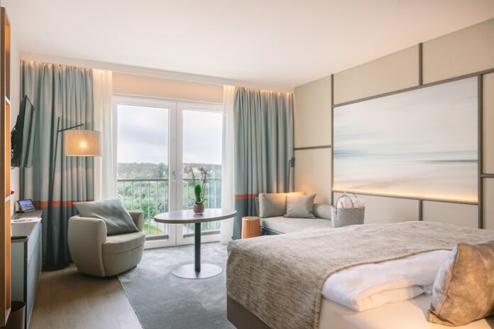 Hotelzimmer in sanften Farben mit Bett, Tisch und Sessel und Blick nach draußen