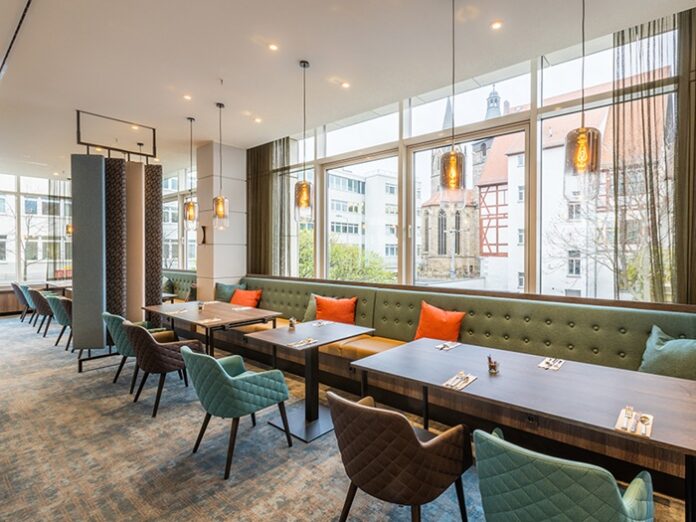 Restaurant mit Polsterbänken, Tischen und Stühlen und breiter Glasfront mit Blick auf die Erfurter Altstadt