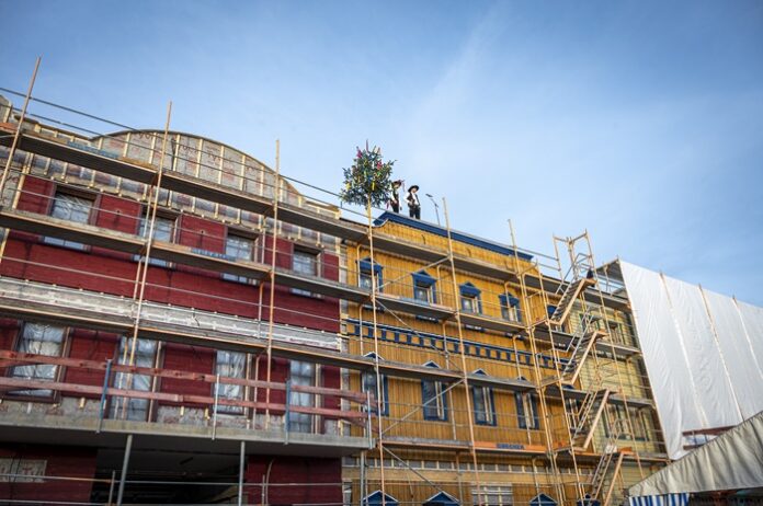 Eingerüstetes Gebäude mit Tannenbaum auf dem Dach zum Richtfest