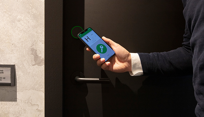 Ein Mann hält ein Smartphone mit digitalem Hotelschlüssel vor eine verschlossene Tür.