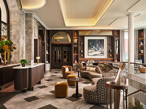 Elegante Lounge im Rosewood Munich mit Marmorfußboden, komfortablen Design-Sesseln, Holzvertäfelung, Kunstwerken an der Wand und großen Fenstern.