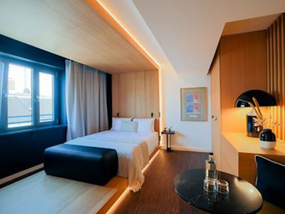 Designorientiertes Zimmer im Bob W an der Münchner Freiheit mit Doppelbett, warmen Holzoberflächen, indirekter Beleuchtung und kompakter Arbeits- und Kaffeestation.