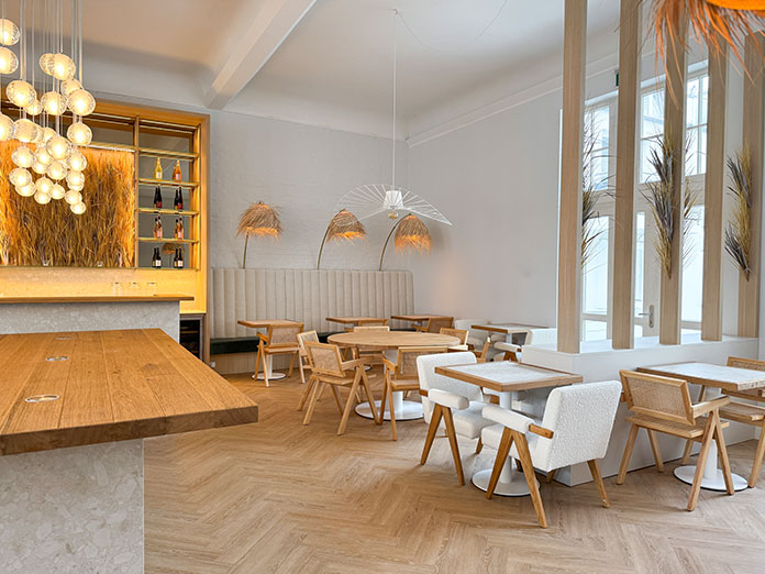 Heller Restaurantbereich der Villa Astoria in Kühlungsborn mit maßgefertigten Tischen, natürlichen Materialien und Dekton-Ava-Elementen.